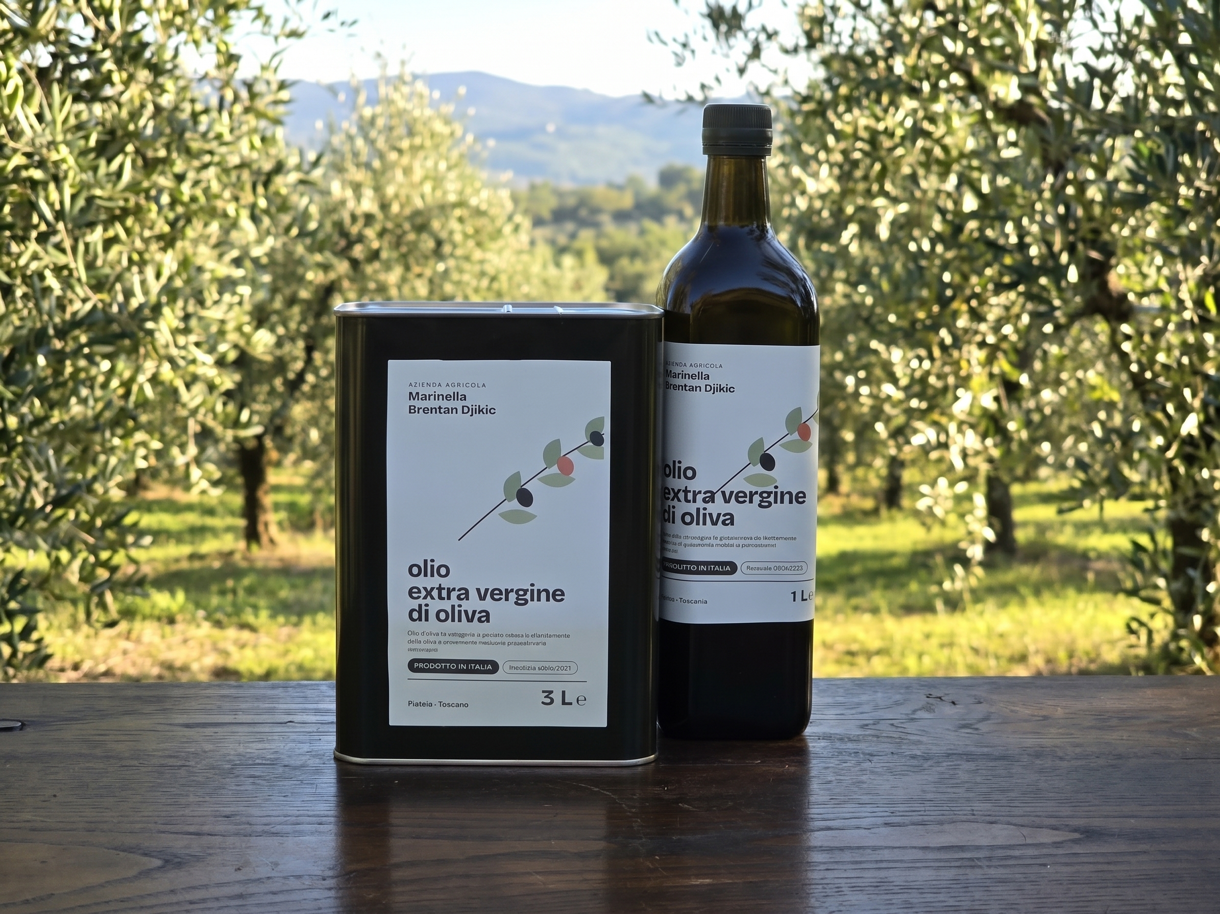 Stagna da 3 litri e bottiglia da 1 litro di olio extravergine dell'azienda, raccolta 2026/2027, su un tavolo in legno davanti a un muro in pietra